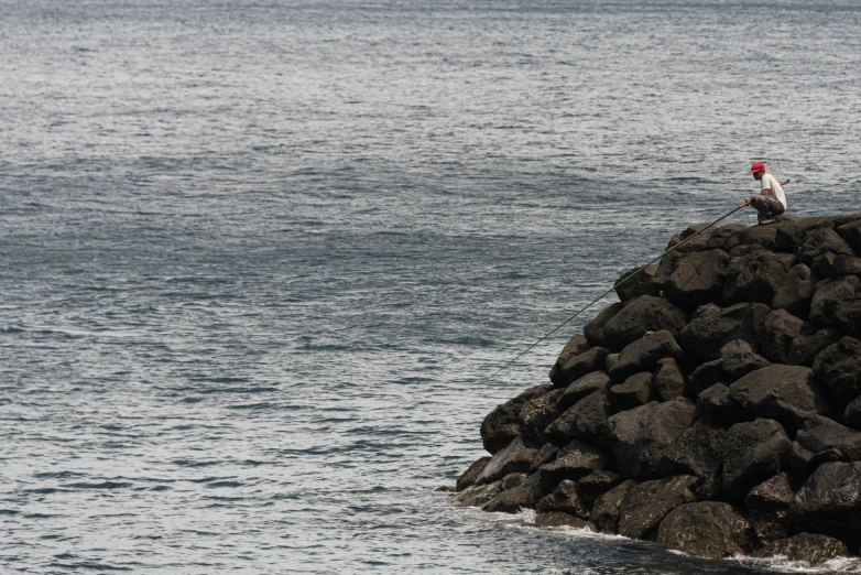 a person is fishing off the edge of rocks near the water