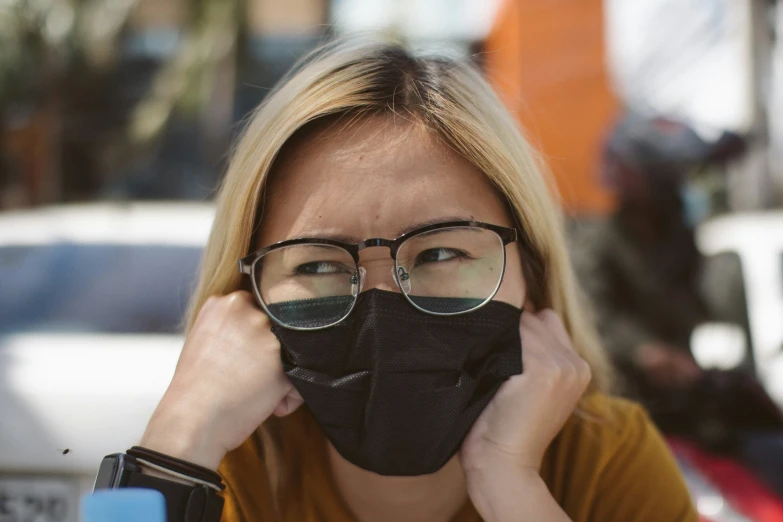 a woman wearing glasses and a face mask holds her mouth up to the camera