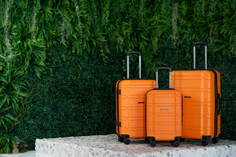 three orange luggage bags sit side by side on a pedestal