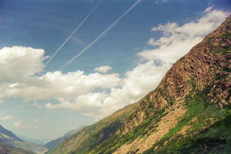 two airplanes flying over some cliffs with grass and blue sky