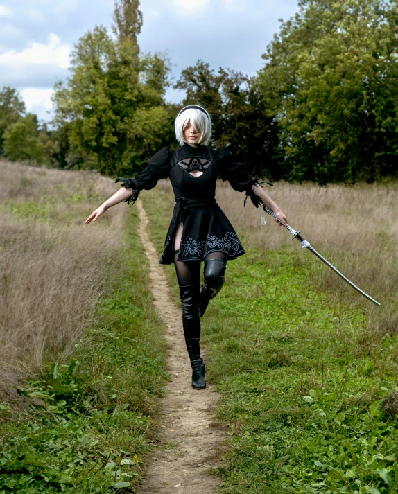 a woman dressed in all black holding two sticks and walking through the grass