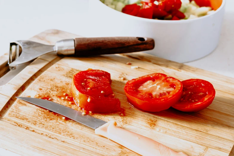 a cut tomato sitting on top of a  board next to some chopped vegetables