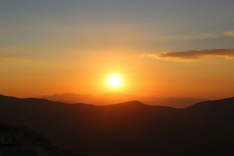 a sun rising over mountains with a dark sky