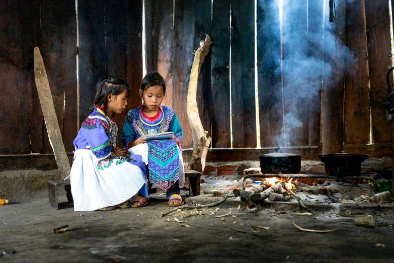 two women sit by a fire as they look at soing