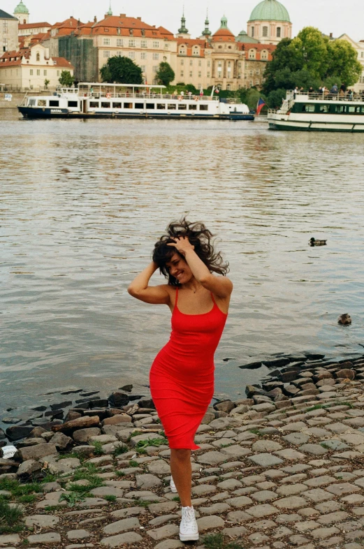 woman in red dress walking by water with boat in the background