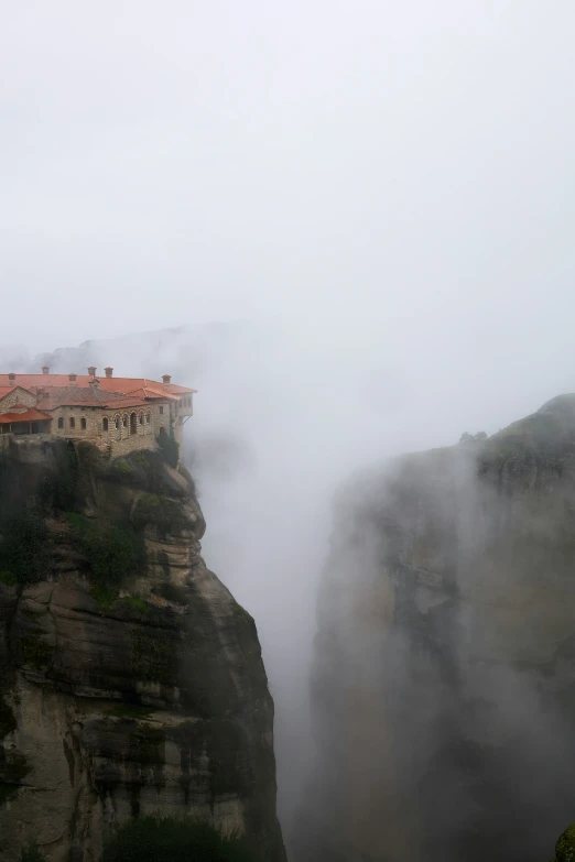 a foggy mountain side with a large cliff and a small town