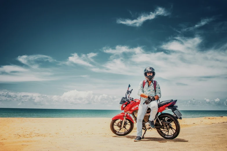 man standing beside two red motorcycles on the beach