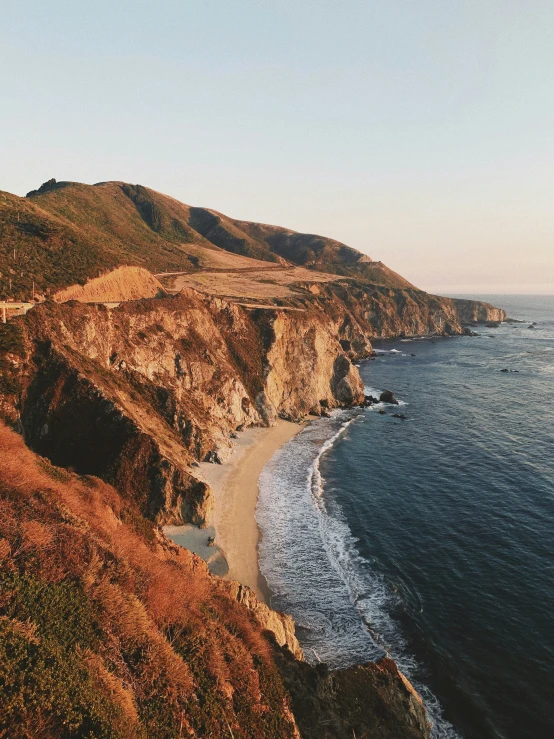 a beach with brown cliffs and ocean with two lighthouses