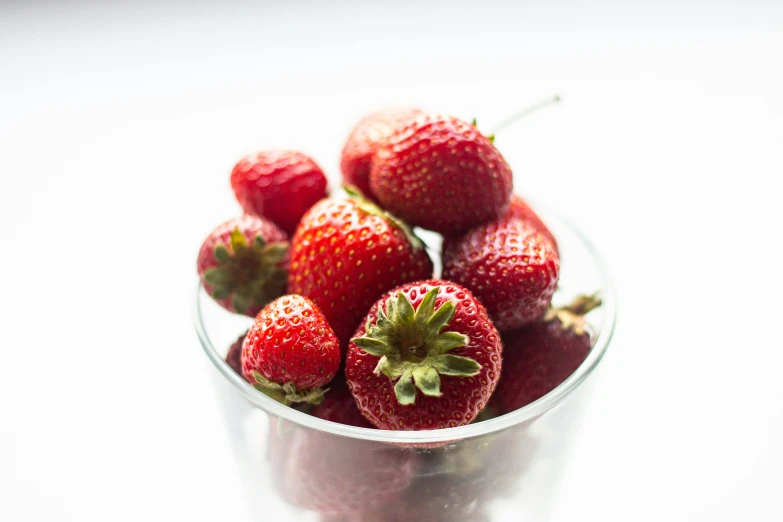 a glass bowl full of fresh strawberries on the counter