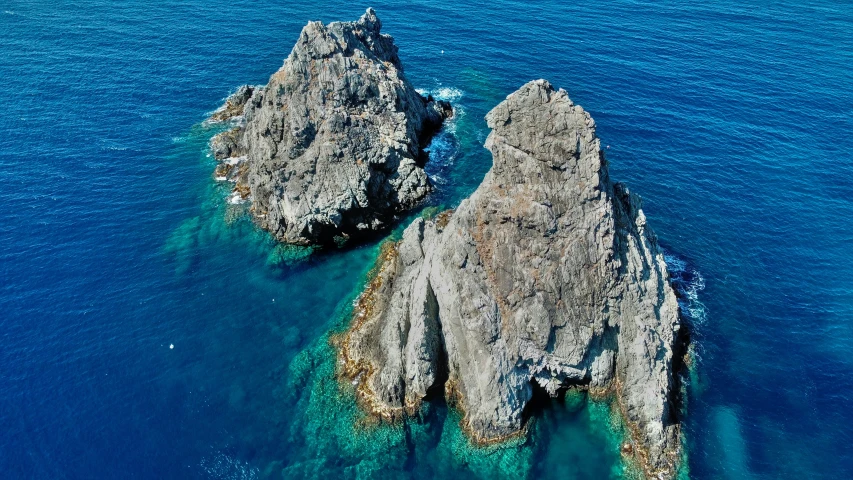 three rocks surrounded by blue water and cliffs