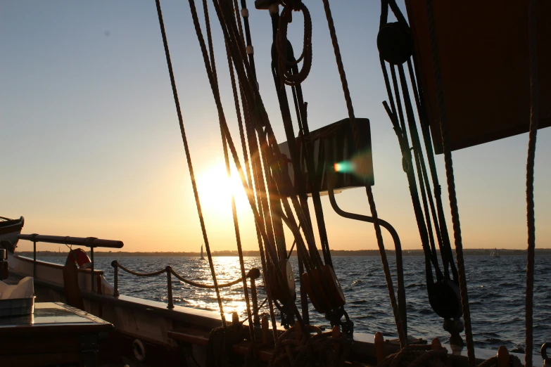 a sun setting over the ocean and the masts of a boat