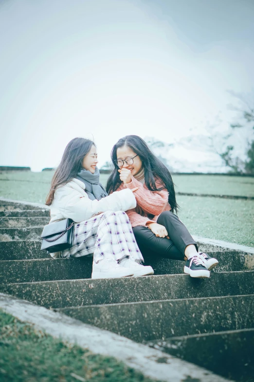 two young women sitting on concrete stairs with their hands together