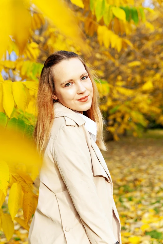 a woman poses near a leafy tree in the fall