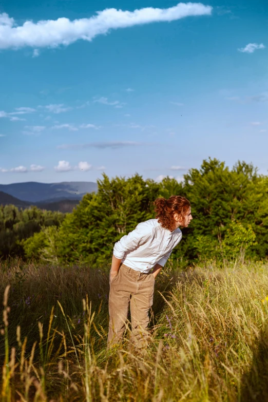 a woman stands alone in a tall grass field with trees