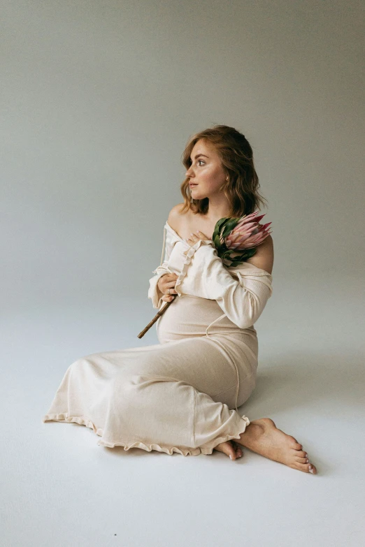 a woman sitting on the floor wearing a white dress and holding a floral bouquet