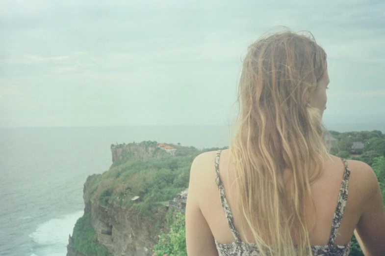 a woman with long hair stands near the ocean