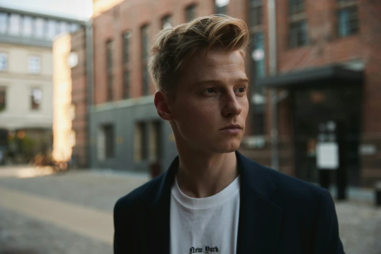 a man with blonde hair stares off in front of a large building