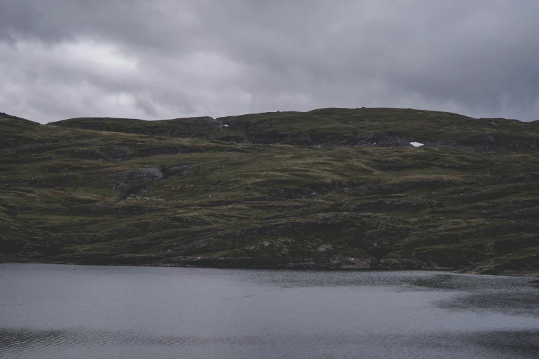 some green hills some water and a grey cloudy sky