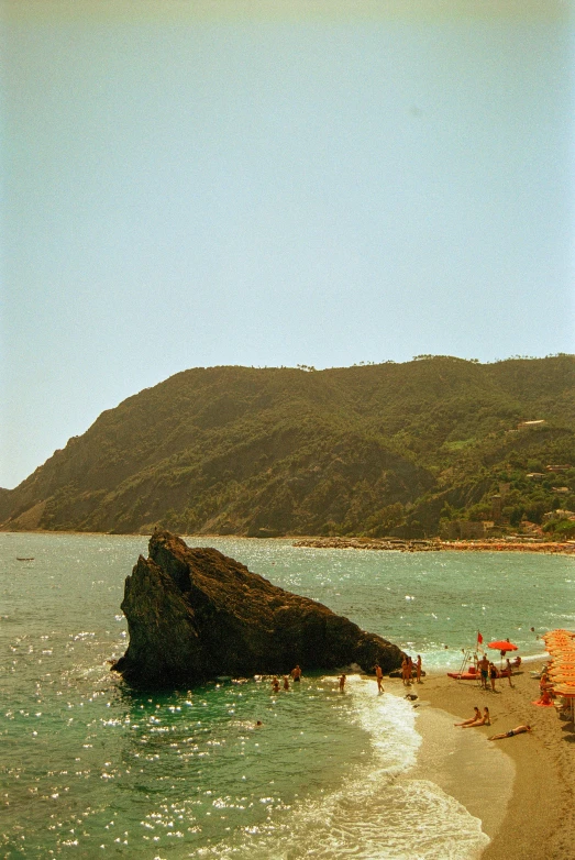 people on the beach and by the water in front of mountains