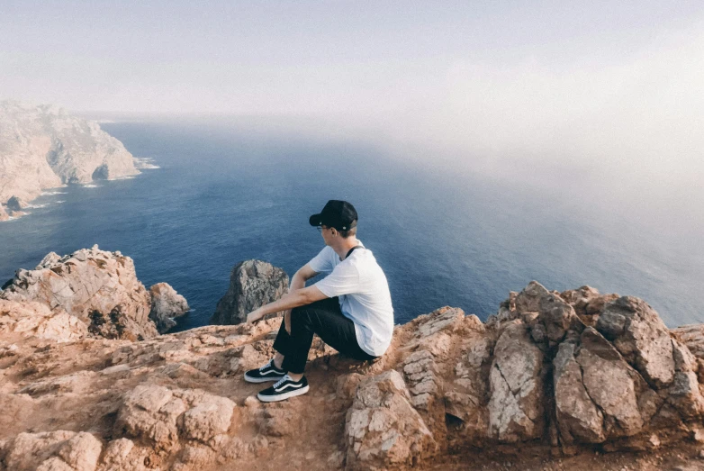 a man on top of a mountain sitting near the ocean