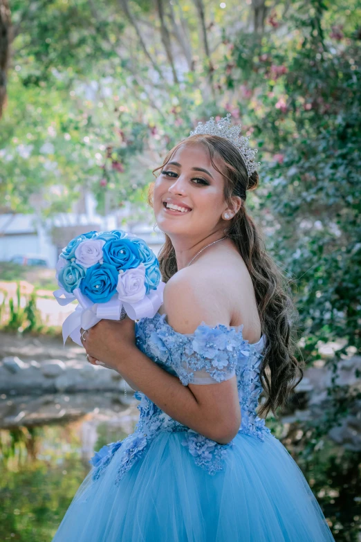 a woman in a blue dress holds a bouquet and smiles for the camera