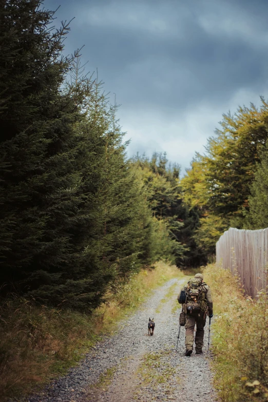 man hiking down dirt path next to fence with backpack