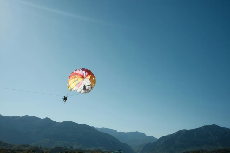 someone parasails through a mountain landscape on a sunny day