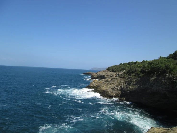 a view from above, of water, cliff and shoreline with hills in the background