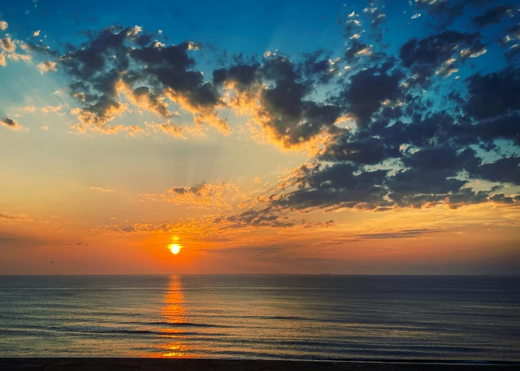 the sun is setting over the ocean on a cloudy day