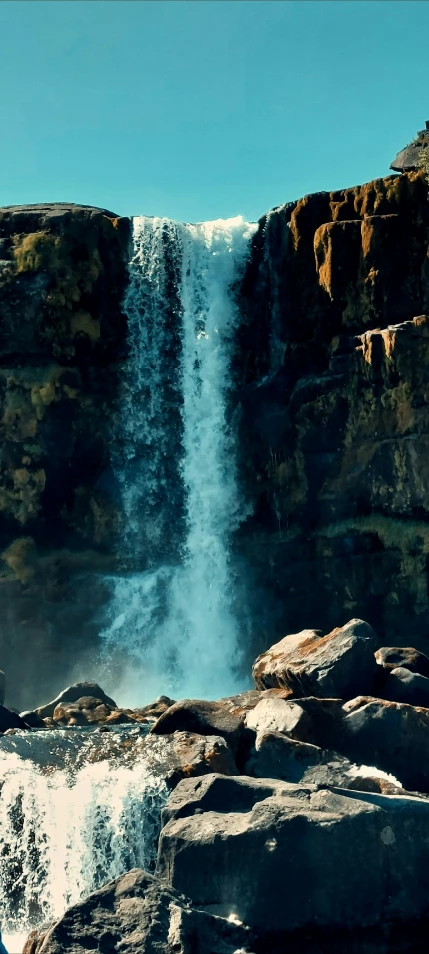 a waterfall cascades over large rocks into the sky