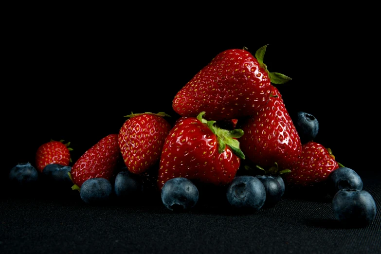 a pile of red strawberries, blueberries and blackberries