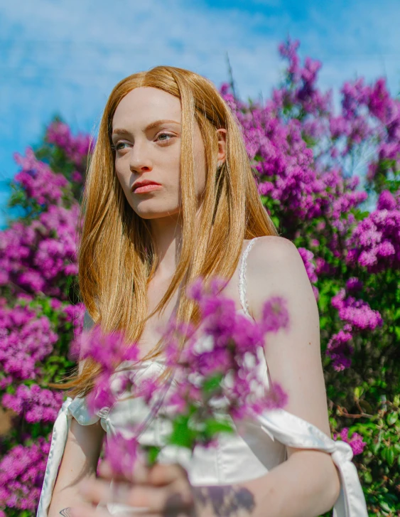 a beautiful young woman posing with purple flowers in front of her