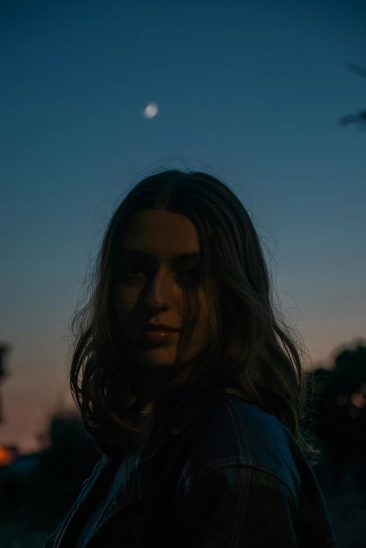 a woman standing at night with a crescent shaped moon in the distance