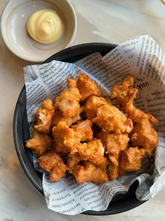 a dish of fried tater tots with a small container of mayonnaise