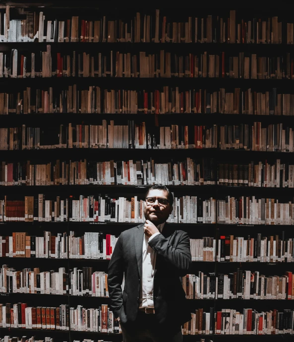 a man standing in front of bookshelves with his hands to his mouth