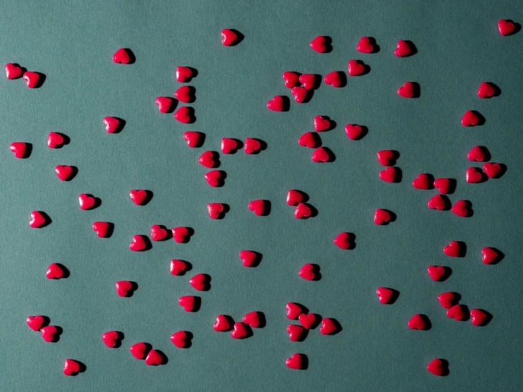 red heart candies are scattered on a teal green background