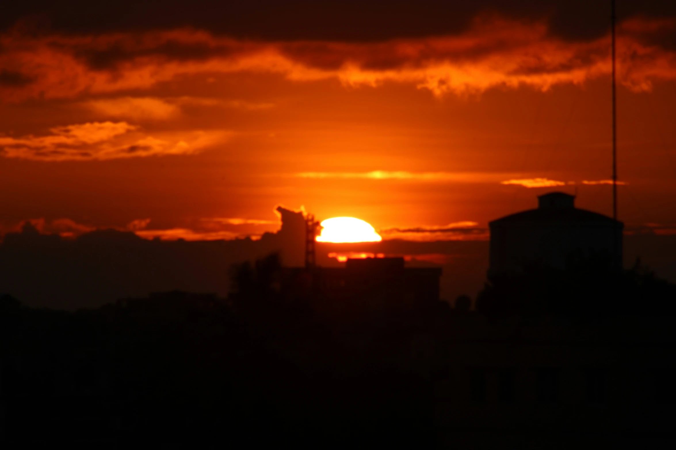 the sun sets in the horizon behind an industrial area