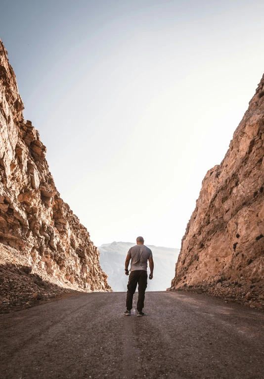 a man walking down the road in between some large rocks