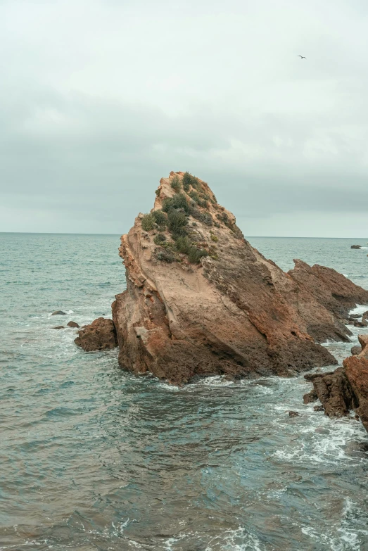 an aerial view of a large rock sticking out from the ocean