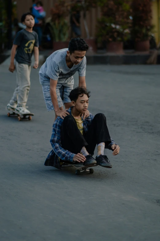 two boys on skateboards going down the street with one boy sitting on his back