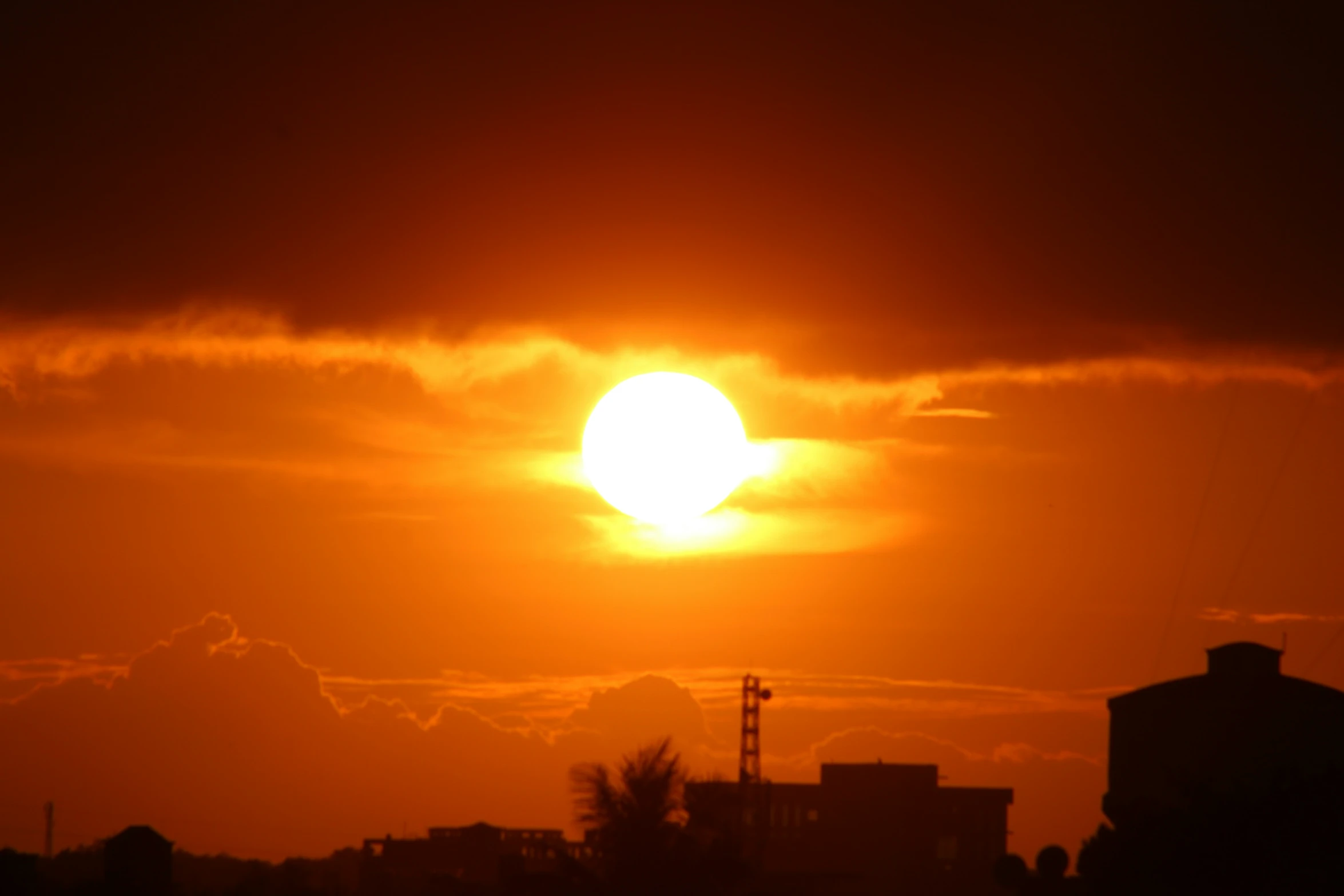 the sun setting over city buildings in a cloudy sky