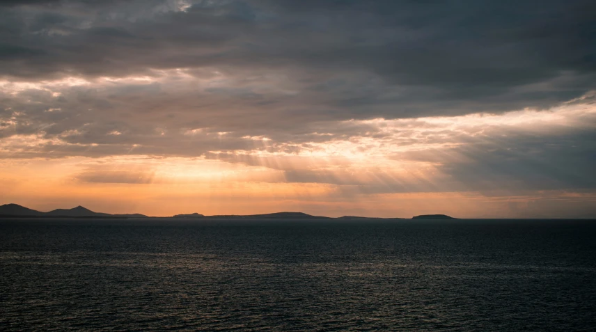 dark cloudy skies and the sun shining over the water