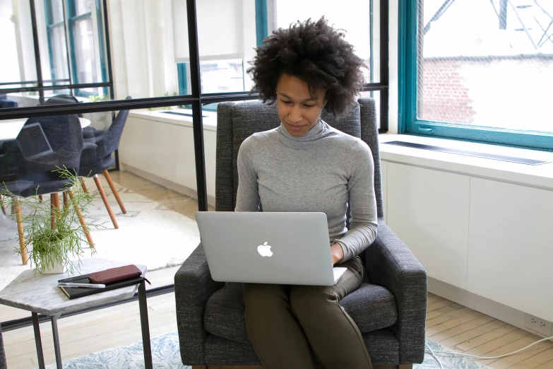 the woman is sitting in a gray chair with her laptop