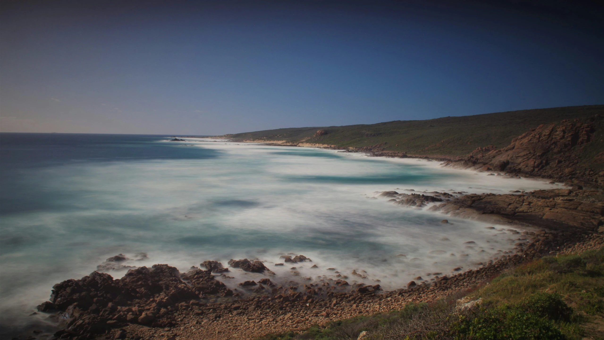 the ocean is blue and white with some green grass on the shore