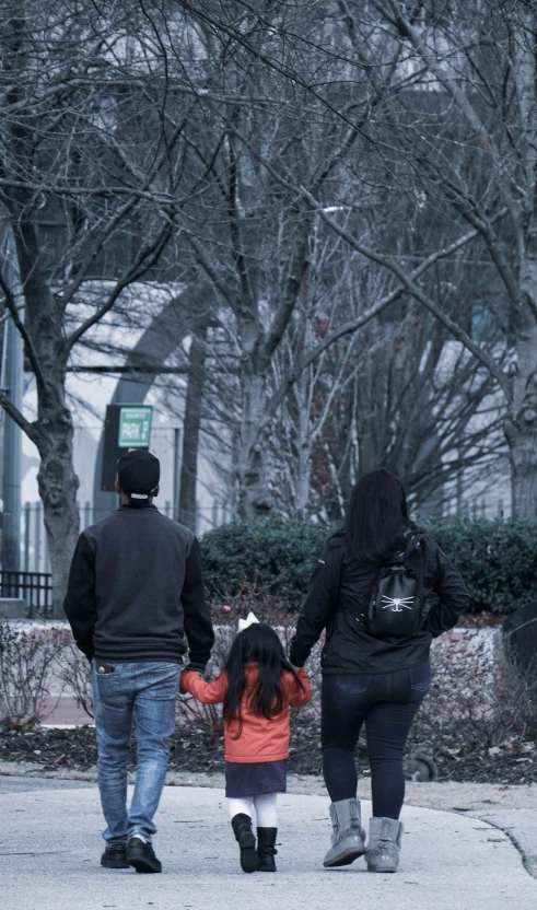 two adults and a child walking with a dog on the street