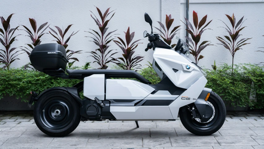 a modern motorbike sits on a concrete slab next to plants