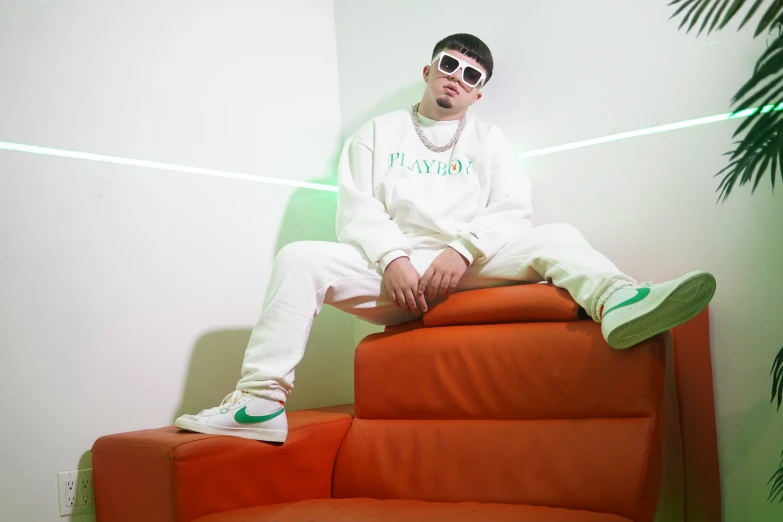 the young man is wearing sunglasses sitting on an orange couch