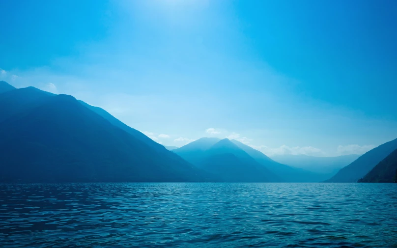 an ocean scene with mountains and the sun above