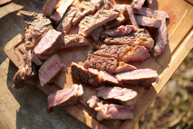 sliced steak on a wooden  board with other meats