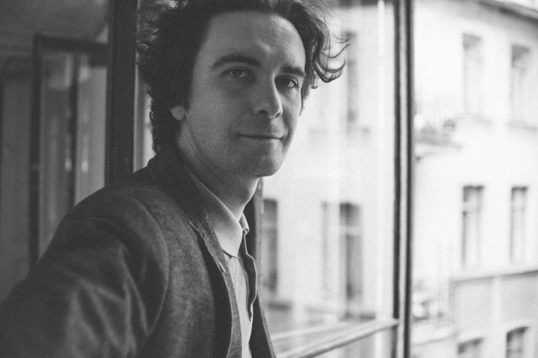 black and white pograph of man with long hair standing in front of a glass wall